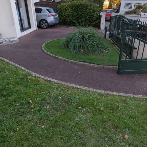Allée en enrobé nettoyée et désherbée devant une maison, îlot de pelouse et graminée