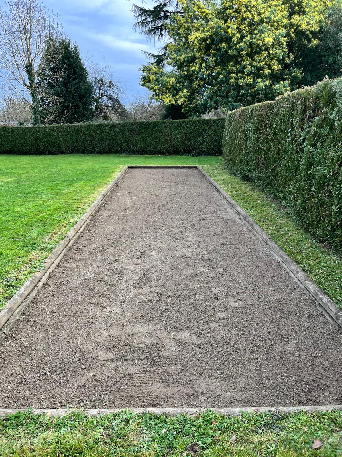 Terrain de pétanque désherbé et ratissé, bordé de haies de charmille taillées