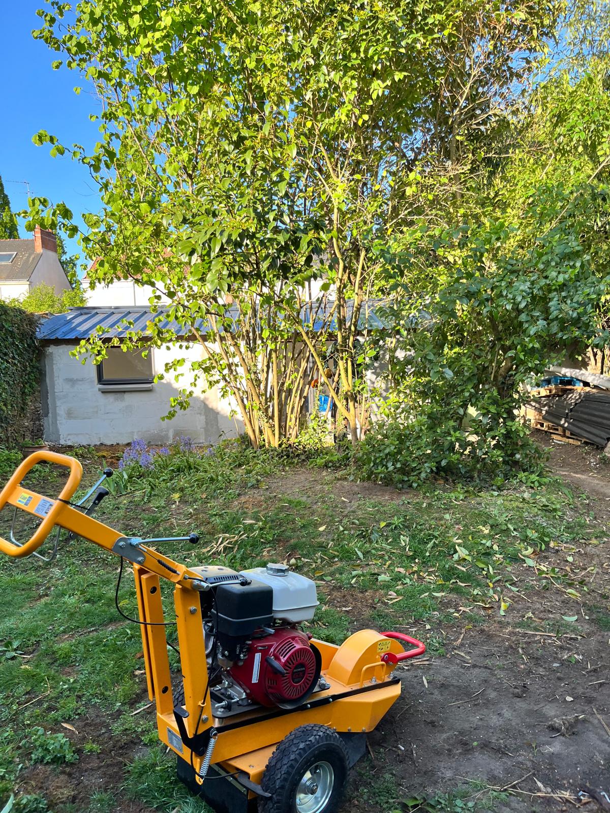 Machine thermique jaune installée dans un jardin au pied d'arbustes à arracher
