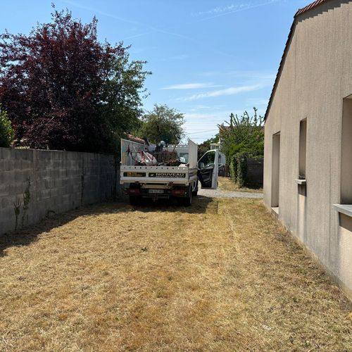 Pelouse jaunie et clairsemée le long d'une maison, camion benne stationné au fond