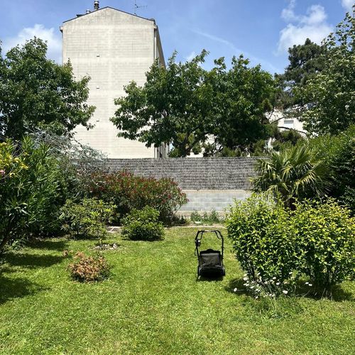 Tondeuse posée sur une pelouse tondue dans un jardin urbain arboré