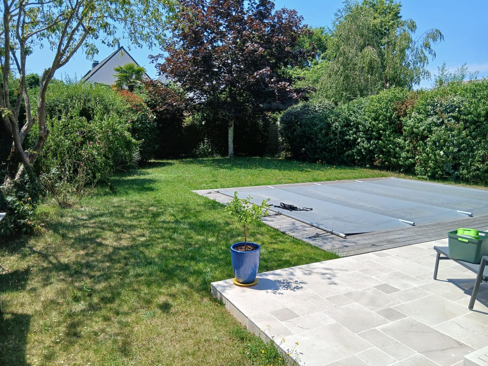 Pelouse tondue autour d'une piscine bâchée et d'une terrasse en pierre à Nantes