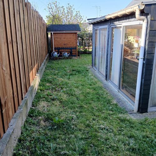 Pelouse clairsemée entre une clôture en bois et une véranda, avant rénovation