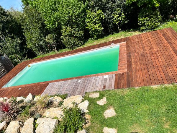 Piscine bordée d'une large terrasse en bois et d'un talus enherbé dans un jardin